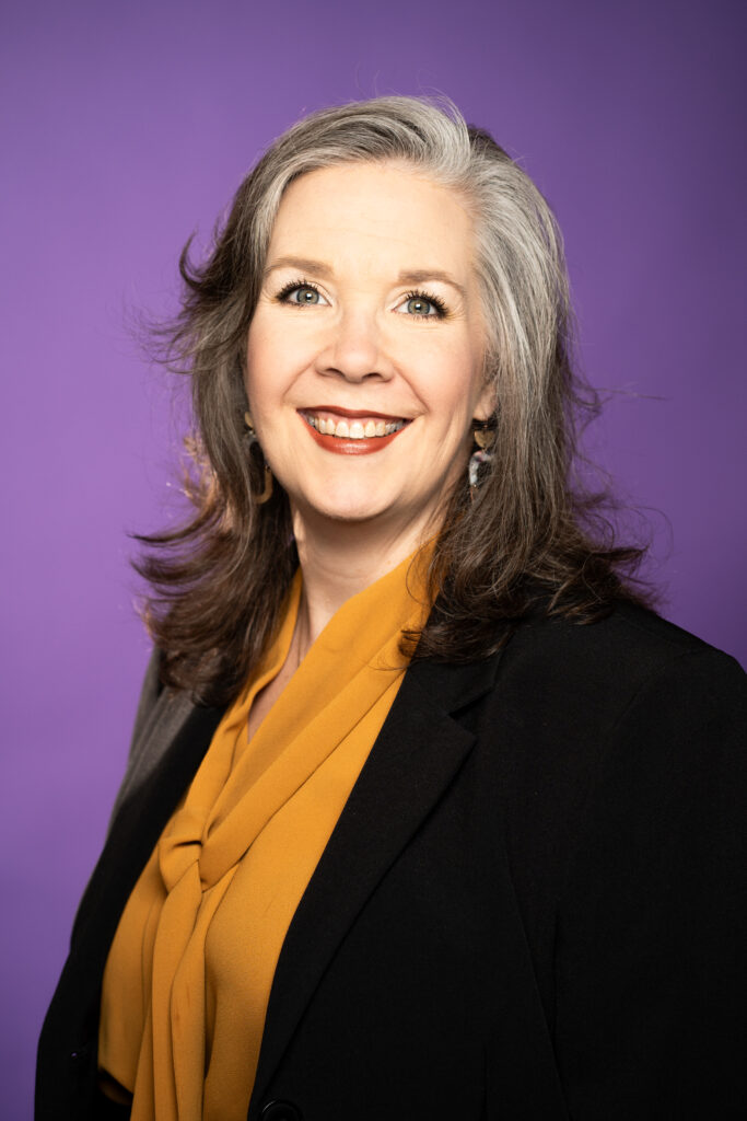 Staci Bell - A picture of a woman in professional clothing in front of a purple background