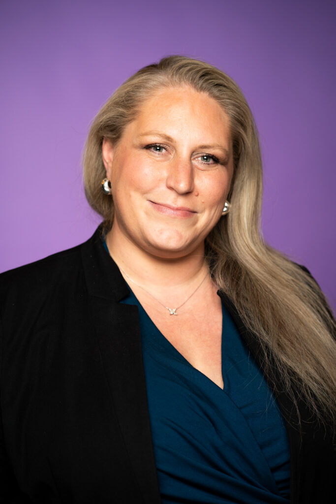 Lara Kennedy - A picture of a woman in professional clothing in front of a purple background
