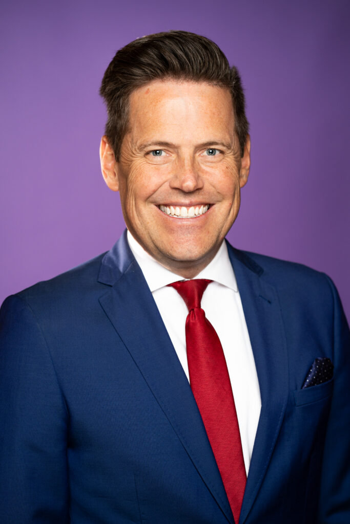 Marty Bodell - A man in a suit in front of a purple background